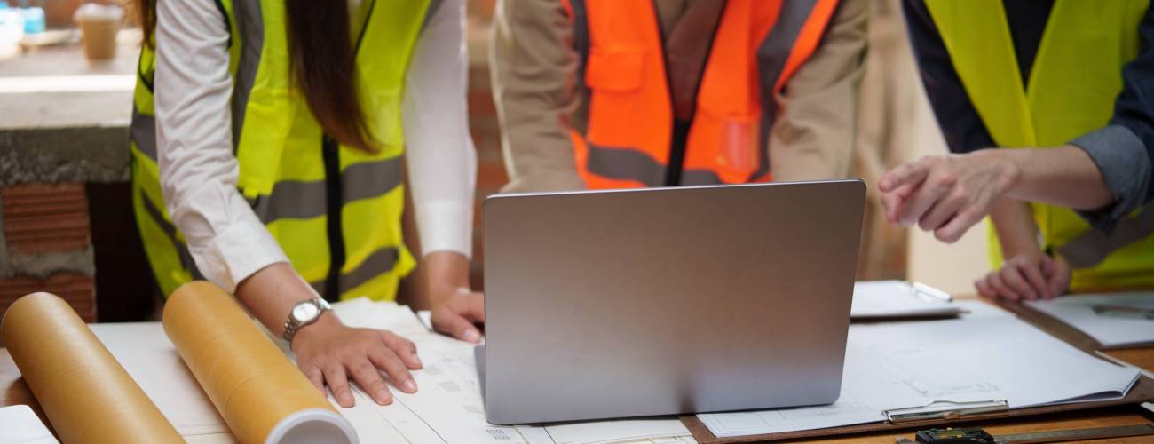 Team of construction professionals analyzing architectural drawings and digital plans on a laptop.